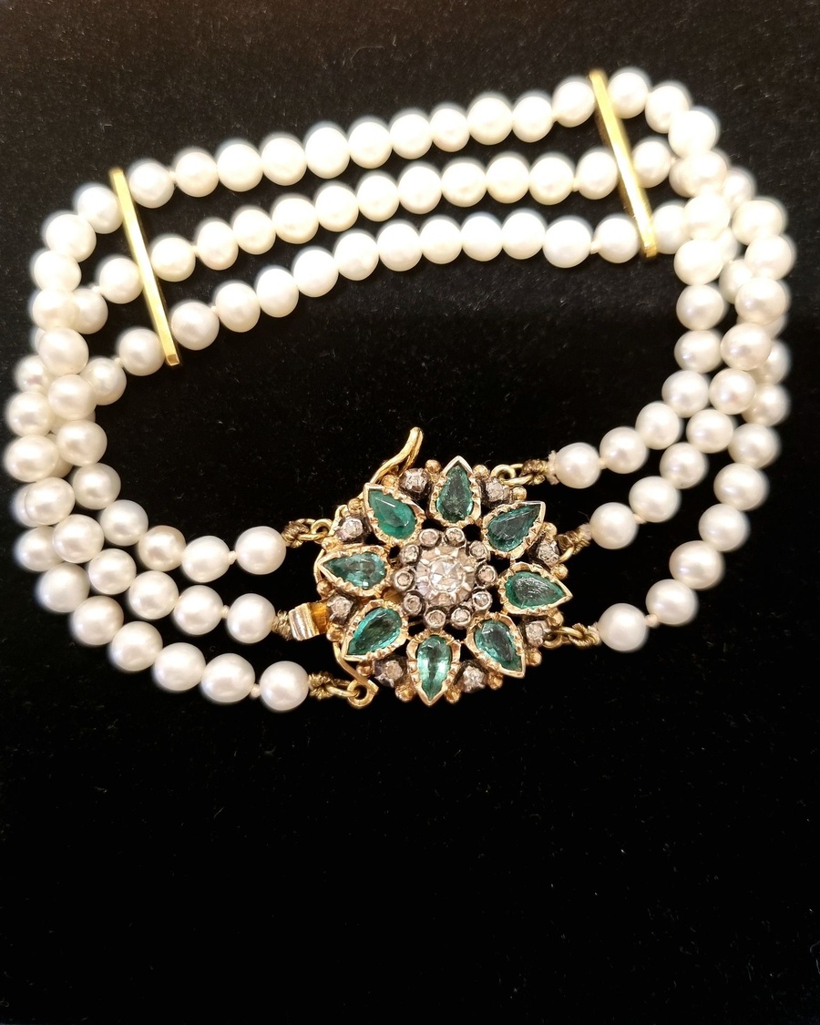 Pearl necklace and antique jewel against a black background
